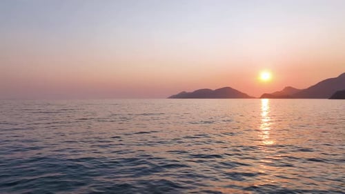 Warm Golden Sunlight Descending Behind Distant Hills Illuminating Tranquil Ocean Surface with Soft
