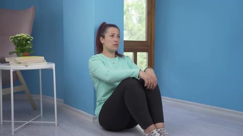Sad Woman Sitting Against Wall in a Blue Room