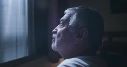 Senior Man Looks Through Window at Night
