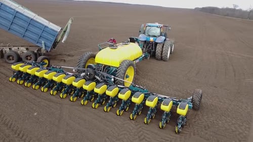 Blue tractor with yellow seeder working on the field in Ukraine OA