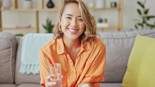 Happy woman, face and drinking glass of water in home, living room and lounge for healthy lifestyle
