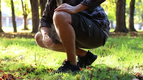 Man spraying tick repellent onto leg in park, closeup