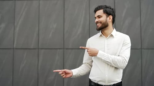 Smiling handsome businessman pointing with fingers at empty space for writing text standing