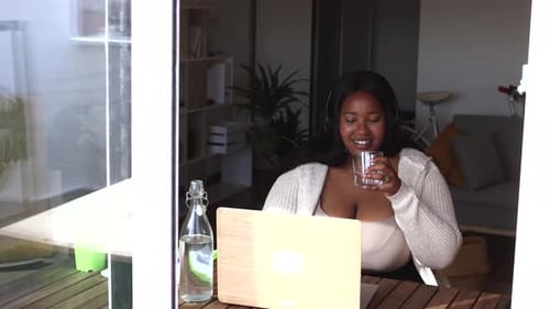 jovem curvilínea trabalha em casa com laptop. Bebendo um copo de água.