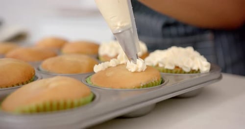 Decorating cupcakes with frosting, person using piping bag in kitchen