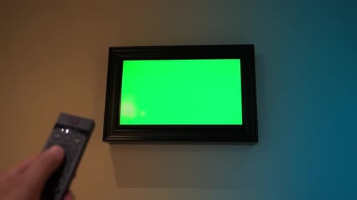 Man Watching TV with a Green Screen in the Living Room Flipping Channels Holding a Remote Control