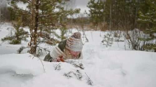 Portrait of Laughing Caucasian Girl Crawling in Snow during Forest Walk