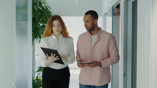 Caucasian Businesswoman and Multiethnic Businessman Walking in Office Discussing Project