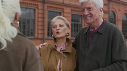 Senior Couple Talking With Friend Outdoors Near Building