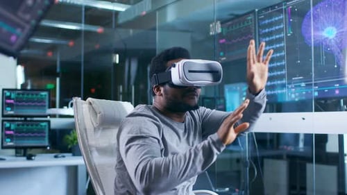 In Laboratory Scientist Wearing Virtual Reality Headset Sitting in a Chair Interacts With Monitors
