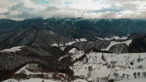Snow-covered Cindrel Mountains under a dramatic cloudy sky, aerial view