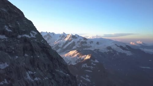 Majestic Aerial View of a Steep Rocky Cliff Face with Distant Snow Covered Peaks