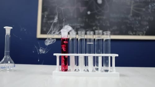 Los tubos de ensayo se mantienen erguidos mientras uno emite humo blanco a partir de un líquido rojo, una fascinante reacción química en p