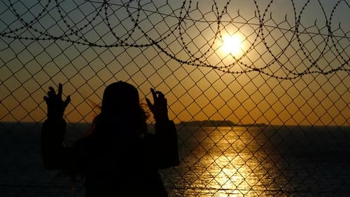 Girl Refugee Looking at Sunset Behind Barbed Wire