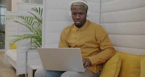 Young African American Businessman Wearing Headphones Working with Laptop in Creative Office