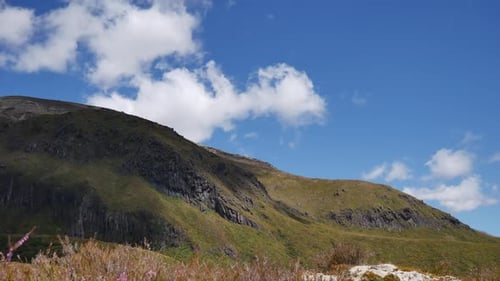 Time-lapse: Clouds blow over tussock green grass on volcanic rock hill