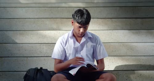 A male high school student in a white school uniform is sitting and studying alone in preparation