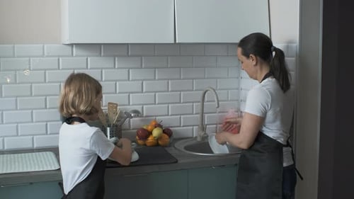 Child and Adult Washing Dishes Together in Kitchen