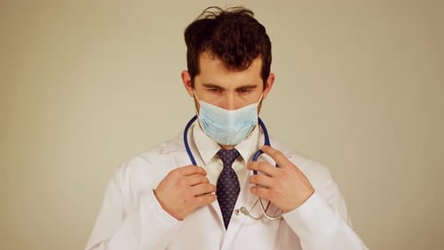A doctor in a white coat and mask adjusting a stethoscope
