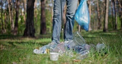 Un hombre con una bolsa de plástico recoge basura en el bosque empalándola en un palo