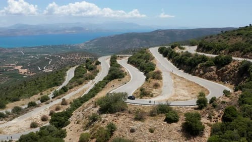 Car Going Down On A Winding Road By The Mountain On A Sunny Summer Day In Peloponnese, Greece. - aer