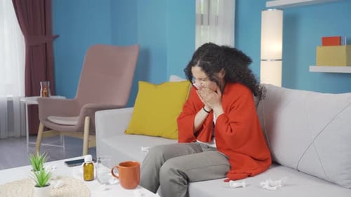 Woman with Cold Sits on Couch Blowing Nose