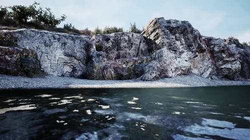 Serene Riverbank Scene with Rocky Cliffs and Calm Water During Daylight