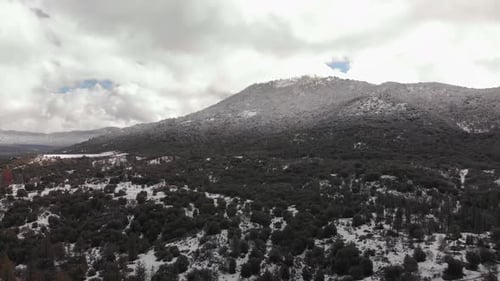 Aerial shot of mountain and valley covered in fresh snow, with storm clouds looming in the backgroun