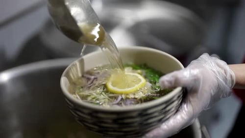 Un chef prépare une soupe vietnamienne traditionnelle PhoBo versant un délicieux bouillon chaud dans un bol avec des nouilles de riz