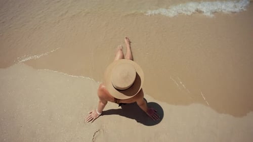 Blonde Frau mit schwarzem Bikini-Strohhut, Blick von oben auf ein Mädchen, das am Meeresstrand auf einer Insel mit Meer liegt