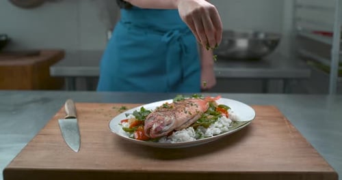 Chef Sprinkling Herbs on Fish Dish