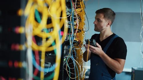 Young man in uniform testing internet equipment by using special device in server room