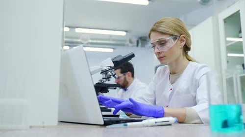 Scientists Working with Microscopes and Laptops in Lab