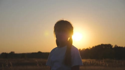 Portrait of Little Smiling Girl in Grass Field with Sunset at Background