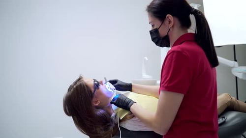 teeth whitening procedure in a dental clinic. female dentist or assistant uses modern equipment.