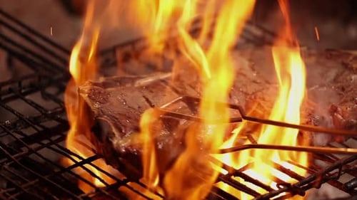 Gros plan au ralenti : un bifteck gras est retourné sur un gril à bois
