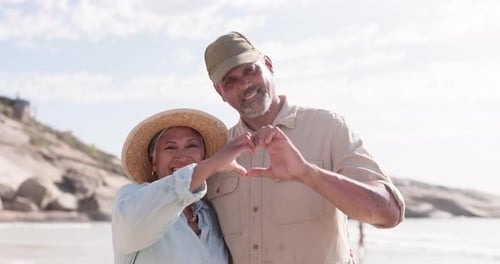 Happy, heart and hands with old couple on beach for love, romance and affectionate