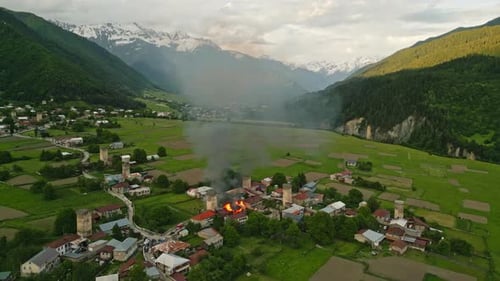 Drone Svan Tower on Fire in Mestia Svaneti Valley Smoke Clouds Rise in Mountain Village Surrounded