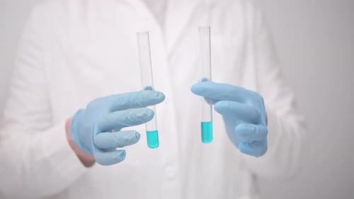 Gloved Hands Pouring Blue Liquid Between Test Tubes