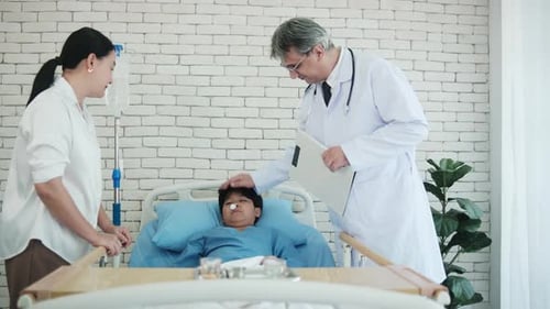 White doctor examines an Asian boy in a hospital ward, consulting with his mum.