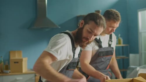 Workers of Moving Company With Uniforms Carefully Packing Dishes at Boxes