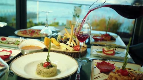 Wine pouring in glass slow motion surrounded by plates of food inside a fine dining restaurant, even