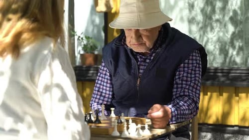 Senior Man Playing Chess Outdoors with Woman