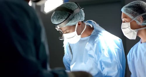 Diverse surgeons wearing surgical gowns operating on patient in operating theatre, slow motion