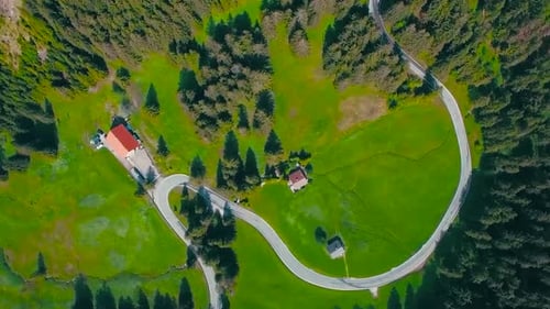 Aerial drone footage of a country rural road in the middle of green fields and trees and houses near