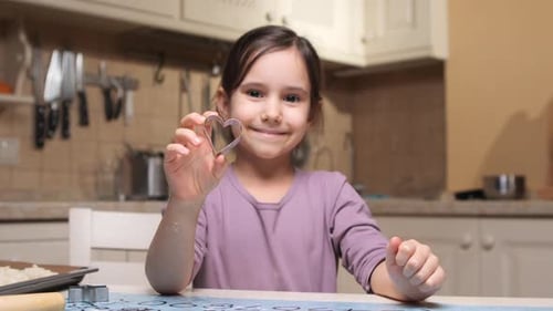 Little Girl Holding Heart Shaped Cookie Cutter in Kitchen