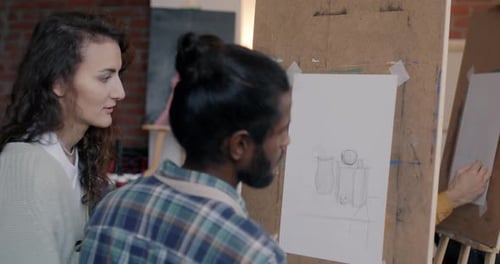 Joven artista profesional que enseña a un estudiante masculino a dibujar explicando durante la clase de arte