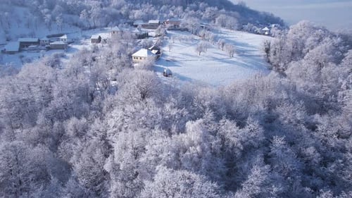 Drohnenaufnahme von schneebedeckten Dorfgebäuden, Wäldern und malerischen Landschaften an einem sonnigen Wintertag