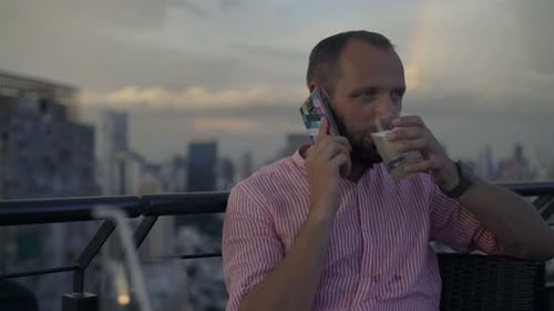 Man Talking on Phone with Drink on Rooftop