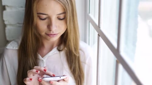 Woman using smartphone near window with natural light
